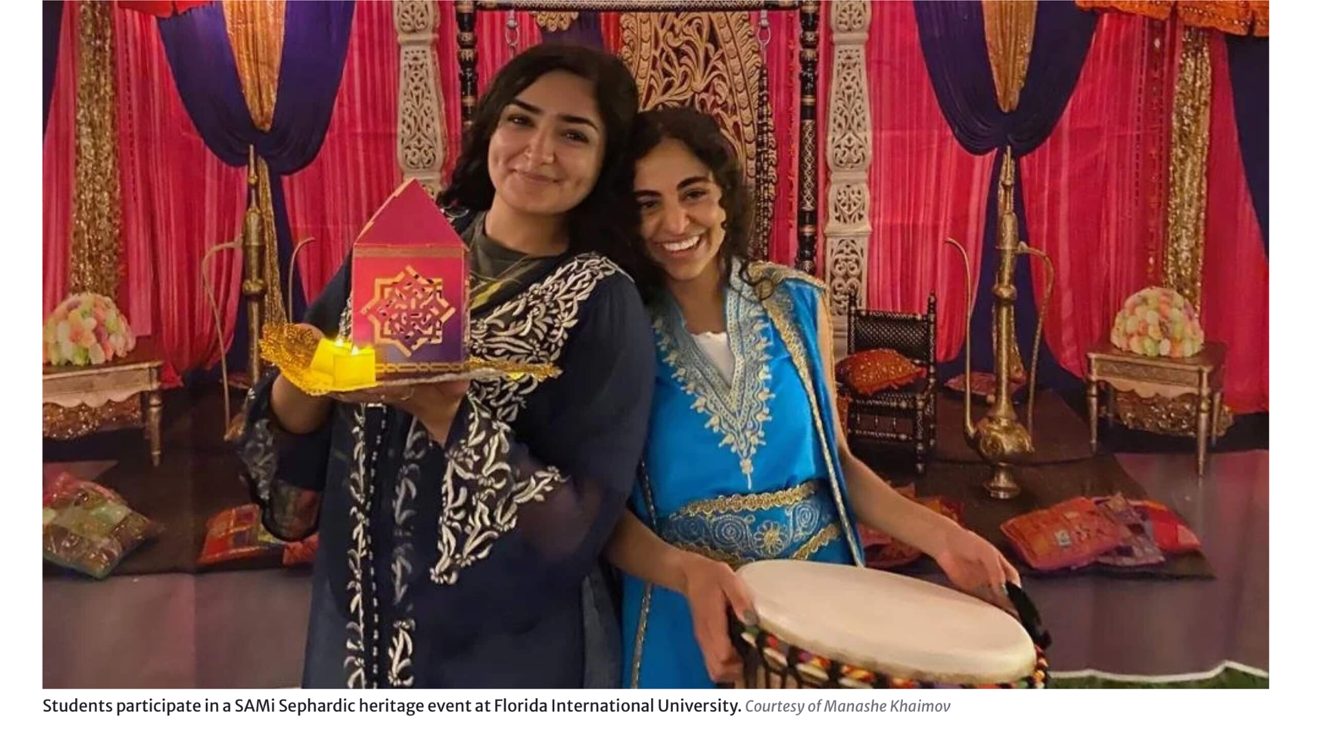 Two students in colorful traditional attire at a Sephardic heritage event, smiling and holding a decorative lantern and a hand drum.