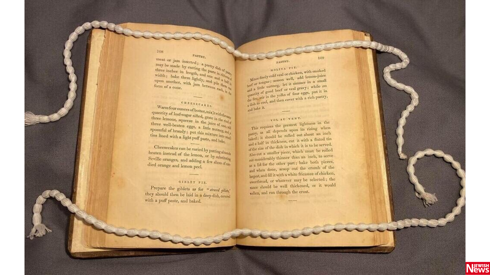 Open antique cookbook with a white cord draped across its pages.